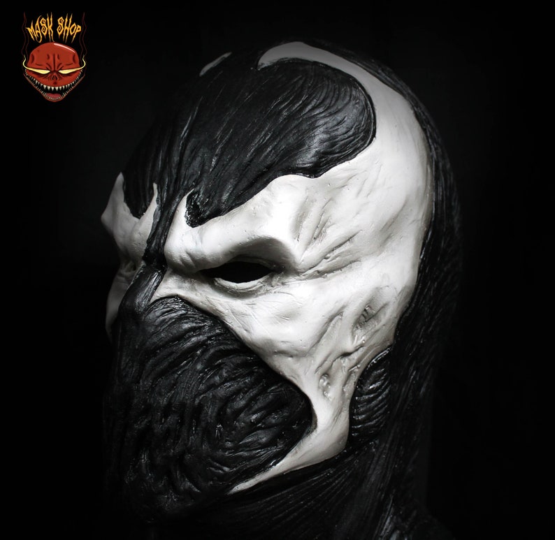 May include: A black and white latex mask of a character with a skull-like face. The mask has a detailed, textured surface and a white skull-like face with a black mouth and eyes.