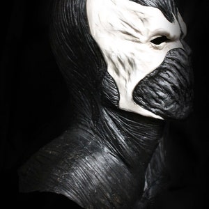 May include: A black and white latex mask of a character with a skull-like face and a long, flowing black cape. The mask has a detailed, textured surface.