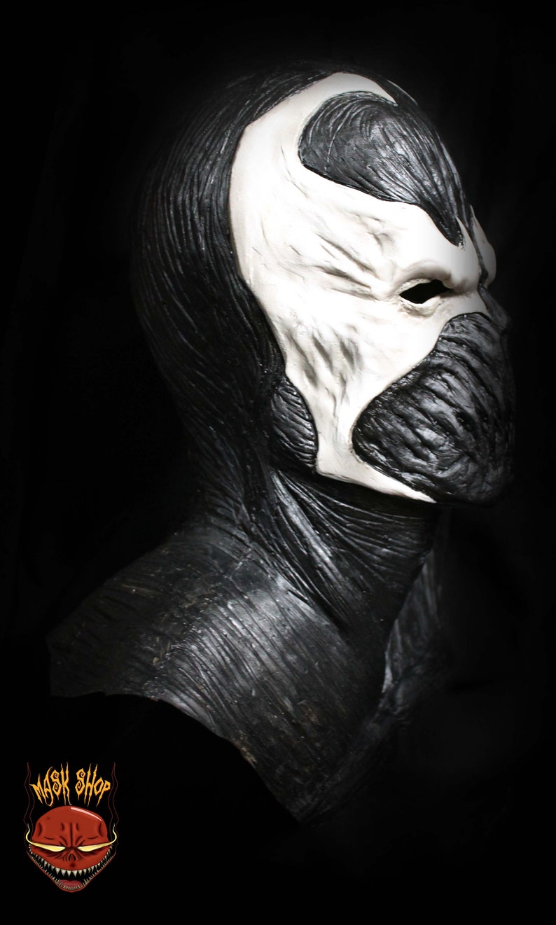 May include: A black and white latex mask of a character with a skull-like face and a long, flowing black cape. The mask has a detailed, textured surface.
