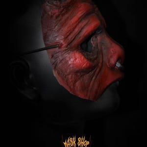 Puede incluir: Una m&aacute;scara de diablo roja con cuernos blancos y una superficie texturizada. La m&aacute;scara tiene una expresi&oacute;n siniestra y est&aacute; dise&ntilde;ada con arrugas y detalles. La imagen incluye el logotipo "MASK SHOP" en la parte inferior.