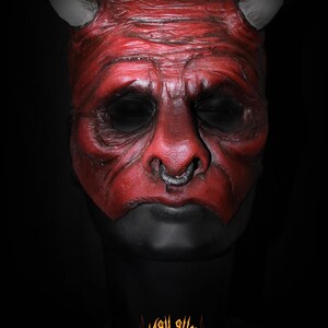 Puede incluir: Una m&aacute;scara de diablo roja con cuernos grises y un aro en la nariz plateado. La m&aacute;scara tiene un aspecto texturizado y cuencas de ojos negras. La parte inferior de la m&aacute;scara es negra. El logo "MASK SHOP" est&aacute; en la parte inferior.