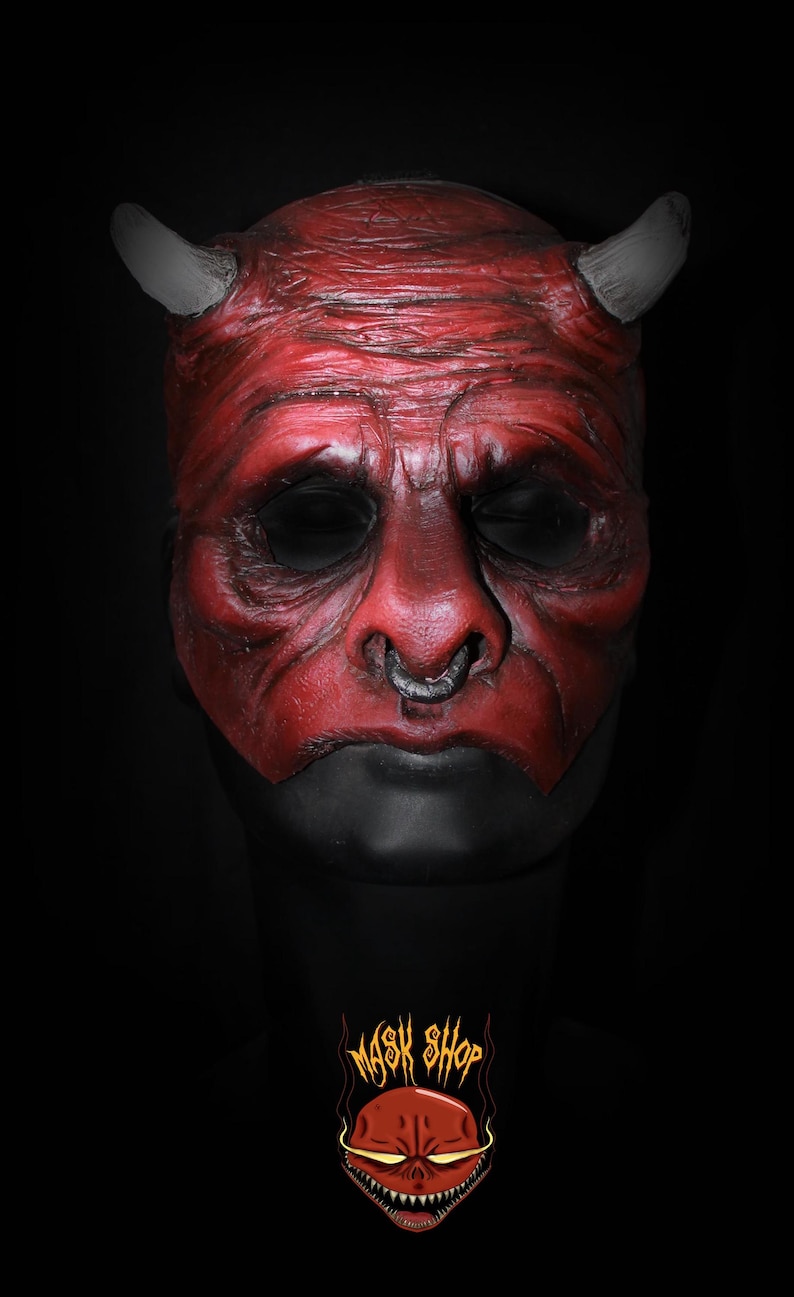 Puede incluir: Una m&aacute;scara de diablo roja con cuernos grises y un aro en la nariz plateado. La m&aacute;scara tiene un aspecto texturizado y cuencas de ojos negras. La parte inferior de la m&aacute;scara es negra. El logo "MASK SHOP" est&aacute; en la parte inferior.