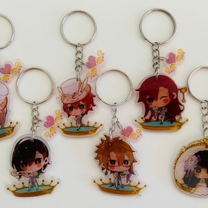 May include: Seven colorful keychains featuring anime characters with different expressions and poses. Each keychain has a silver chain and a clear acrylic charm with a gold crown design. The charms are decorated with pink and gold accents.