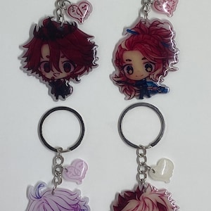 May include: Four anime character keychains with silver chains and heart-shaped charms. The characters are drawn in a chibi style and have different hair colors and outfits. The charms have the word "love" written on them.