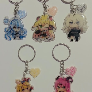May include: Five colourful anime character keychains with silver key rings and charms. The charms are hearts with different colours and designs. The characters are all female and have different hair colours and styles.