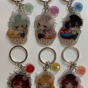 May include: Six colorful keychains featuring anime characters in cupcake-themed designs. Each keychain has a small charm with a number on it.