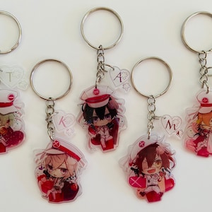 May include: Five colorful anime character keychains with red hearts and white hats. Each keychain has a different character and a letter on a heart charm.