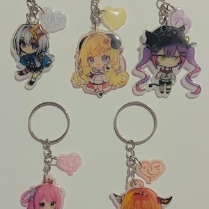 Könnte beinhalten: Fünf bunte Anime-Charakter-Schlüsselanhänger mit silbernen Schlüsselringen und rosa Herzanhängern. Jeder Schlüsselanhänger zeigt einen anderen Charakter mit einem einzigartigen Design und Farbschema.