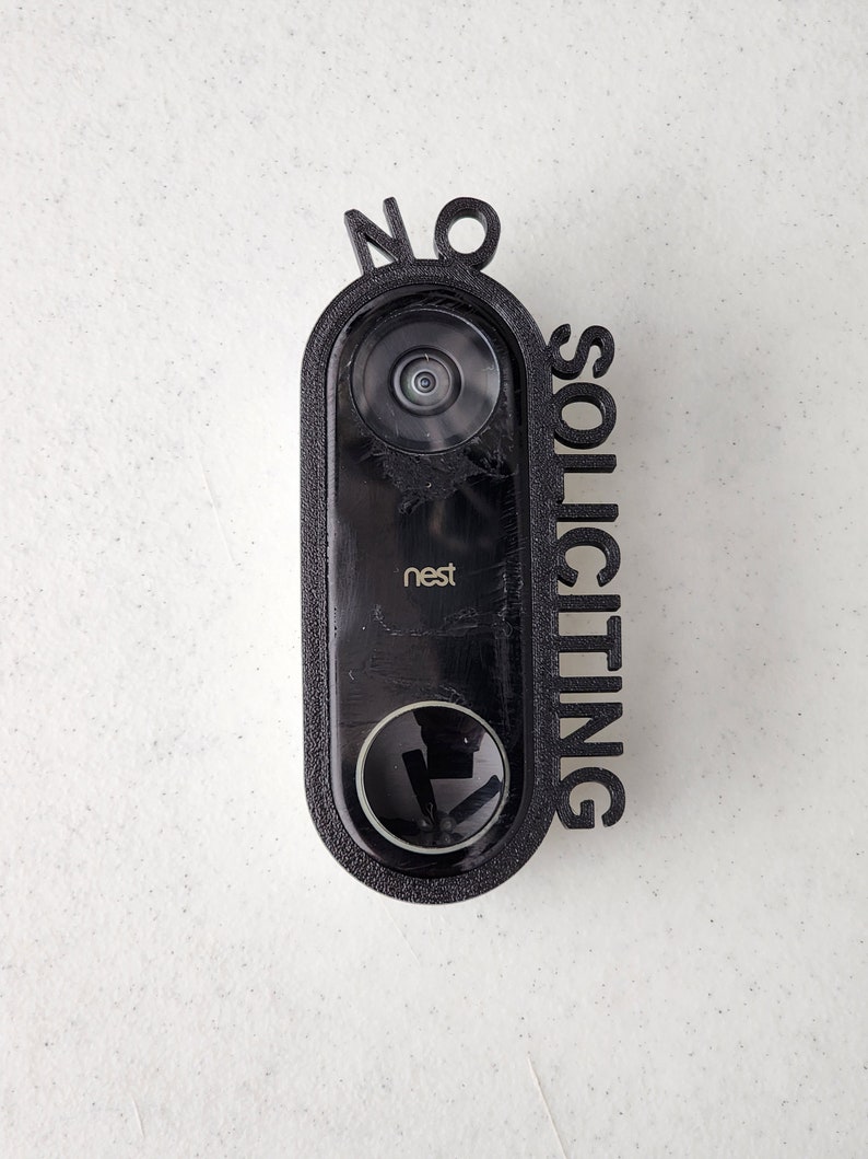 May include: A black Nest doorbell with a 3D printed sign that says "NO SOLICITING" attached to it.