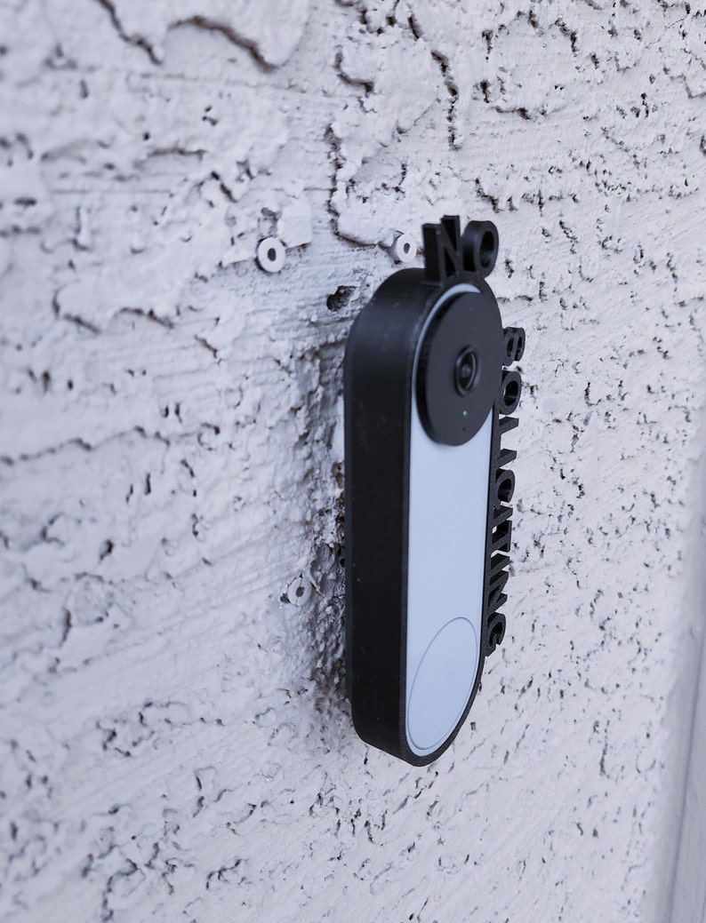 May include: A black doorbell camera with a white faceplate and a sign that says "No Soliciting".