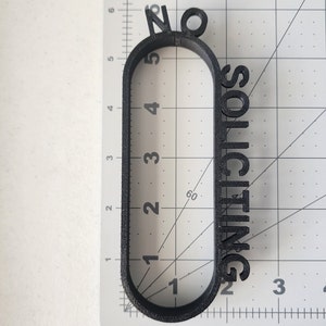 May include: Black plastic sign with the text "No Soliciting" in a rounded oval shape.