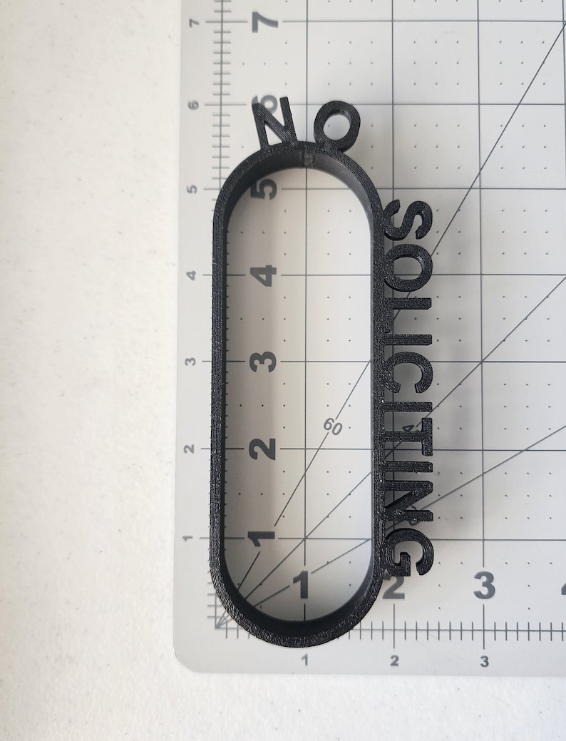 May include: Black plastic sign with the text "No Soliciting" in a rounded oval shape.