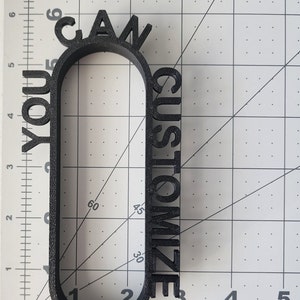May include: A black 3D printed sign that reads "You Can Customize". The sign is shaped like a rounded rectangle with the words wrapping around the edges.
