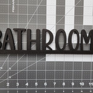Puede incluir: Un letrero de madera negro con la palabra "BATHROOM" en letras grandes y negritas.