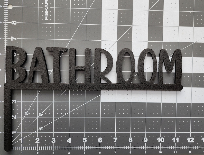 Puede incluir: Un letrero de madera negro con la palabra "BATHROOM" en letras grandes y negritas.