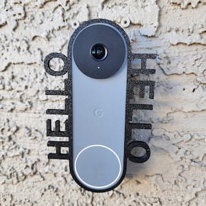 May include: A black and gray Google Nest Hello doorbell with a "HELLO" sign on either side. The doorbell is mounted on a textured wall.