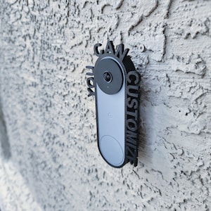 May include: A black custom-made door sign with the words "Gawk" and "Customize" surrounding a white and gray doorbell camera.