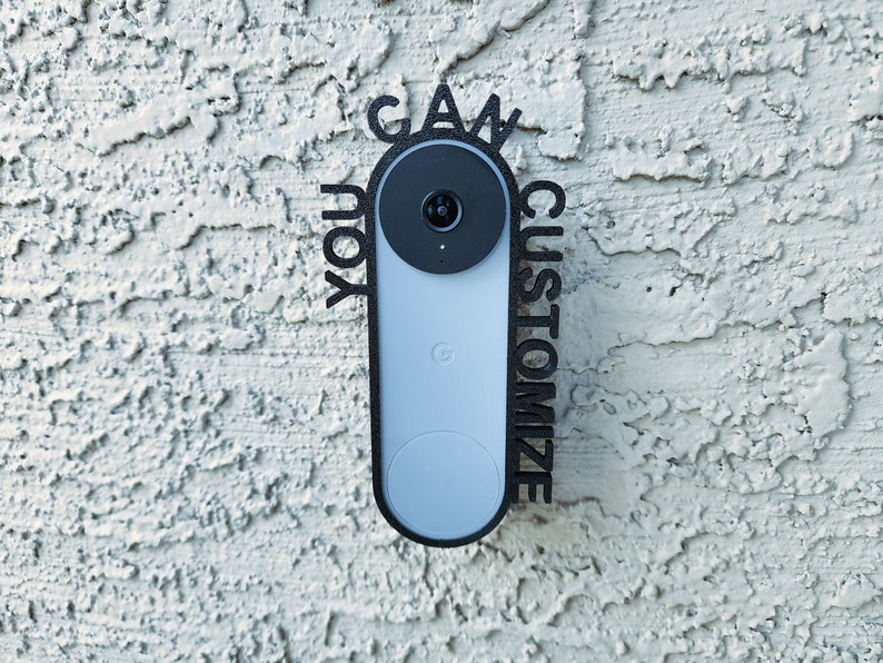 May include: A black and white custom sign that says "You can customize" around a Google Nest doorbell camera. The doorbell is mounted on a white textured wall.