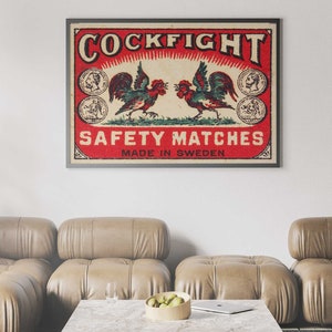 以下が含まれることがあります： 赤い背景に「COCKFIGHT SAFETY MATCHES MADE IN SWEDEN」という文字が書かれた、ビンテージのマッチ箱のラベル。ラベルの中央には、翼を広げて向き合った2羽の雄鶏が描かれている。
