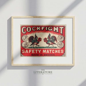 以下が含まれることがあります： 赤い背景に「Cockfight Safety Matches Made in Sweden」と書かれた、ビンテージのマッチ箱のラベル。ラベルには、向かい合った2羽の雄鶏が描かれており、金色と赤色のデザインが施されています。