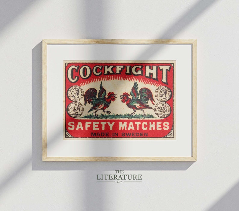 以下が含まれることがあります： 赤い背景に「Cockfight Safety Matches Made in Sweden」と書かれた、ビンテージのマッチ箱のラベル。ラベルには、向かい合った2羽の雄鶏が描かれており、金色と赤色のデザインが施されています。