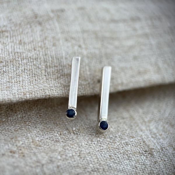Sterling silver bar ear studs with natural dark blue sapphires. Sold as a pair of earrings.
