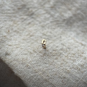 May include: Gold initial charm with a single diamond, featuring the letter "F".
