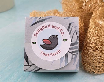 May include: A small, white box with a blue and gray tropical leaf design. The box has a round sticker with a black bird with a red breast and the text "Songbird and Co. Foot Scrub".
