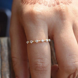 Pode incluir: Um delicado anel de banda de ouro com uma fileira de pequenas pedras preciosas transparentes.