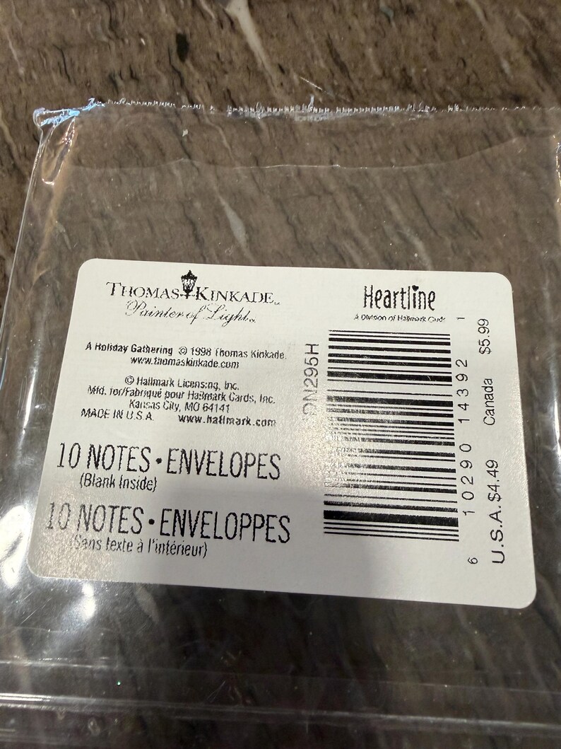May include: A package of Thomas Kinkade "Heartline" note cards and envelopes. The label reads "10 NOTES &bull; ENVELOPES" and "Blank Inside." The package is sealed in clear plastic. The label also includes the text "A Holiday Gathering &copy; 1998 Thomas Kinkade."