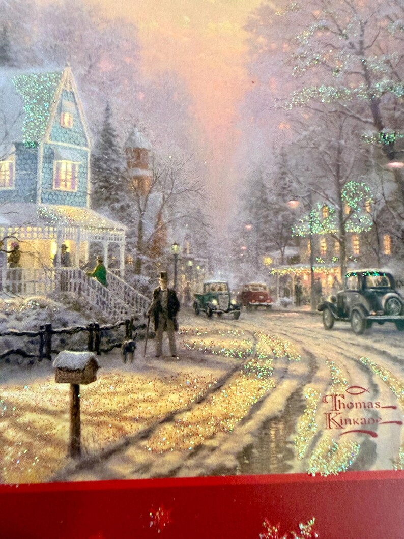 May include: A winter scene painting by Thomas Kinkade depicts a snow-covered street with vintage cars, houses, and figures. The artwork features a man with a dog, a mailbox, and sparkling glitter accents, evoking a nostalgic holiday atmosphere.