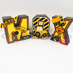 Pode incluir: Letras tridimensionais com tema de constru&ccedil;&atilde;o que soletram "MAX" com um esquema de cores amarelo e preto. As letras s&atilde;o decoradas com ve&iacute;culos de constru&ccedil;&atilde;o, uma placa de zona de constru&ccedil;&atilde;o e uma placa que diz "THREE".