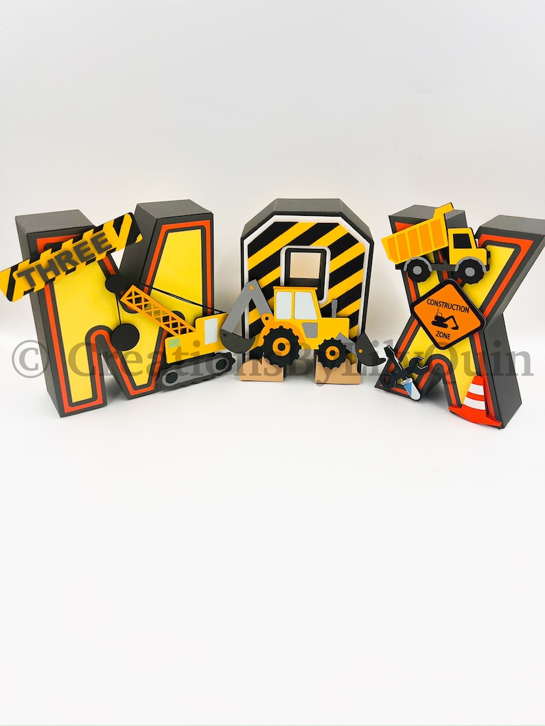 Pode incluir: Letras tridimensionais com tema de constru&ccedil;&atilde;o que soletram "MAX" com um esquema de cores amarelo e preto. As letras s&atilde;o decoradas com ve&iacute;culos de constru&ccedil;&atilde;o, uma placa de zona de constru&ccedil;&atilde;o e uma placa que diz "THREE".