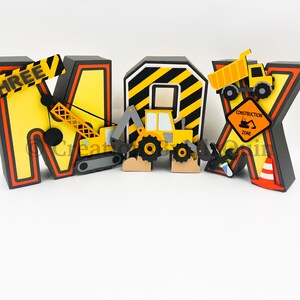Pode incluir: Letras tridimensionais que soletram o nome "MAX" decoradas com ve&iacute;culos de constru&ccedil;&atilde;o e uma placa de zona de constru&ccedil;&atilde;o. As letras s&atilde;o amarelas com listras pretas e bordas pretas. Os ve&iacute;culos s&atilde;o amarelos e pretos. A placa &eacute; amarela com texto preto.