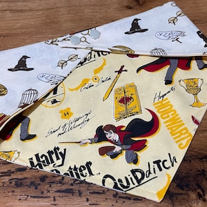 May include: A yellow and white bandana with a Harry Potter theme. The bandana features a variety of Harry Potter imagery, including the Hogwarts crest, a golden snitch, and a Quidditch match. The bandana is made of cotton and is reversible.