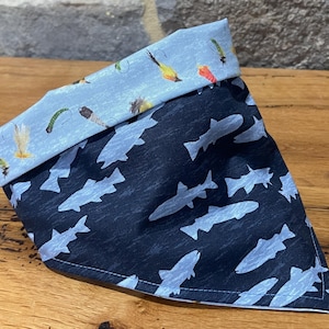 May include: A blue and black bandana with a pattern of fish silhouettes on one side and a pattern of fishing flies on the other side.