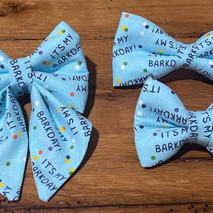 May include: Three blue bow ties with white polka dots and the text "It's my Barkday!" printed on them. The bow ties are made of fabric and are different sizes.