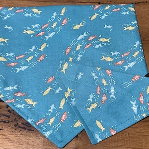 May include: A blue bandana with a pattern of yellow, orange, and pink fish swimming in a wavy pattern. The bandana is folded in half and the pattern is visible on both sides.