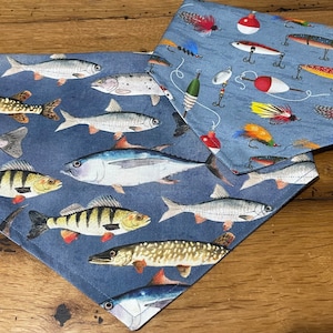 May include: Two blue fabric bandanas with a fishing theme. One bandana features a variety of fish, including a tuna, perch, and pike. The other bandana features fishing lures and bobbers.