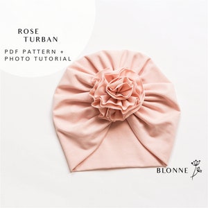 Peut inclure: Un turban rose pâle avec une grande fleur en tissu en forme de rose à trois couches sur le dessus. Le turban est fait d'un tissu doux et extensible. Le texte "ROSE TURBAN" et "PDF PATTERN + PHOTO TUTORIAL" est imprimé en noir en haut de l'image.