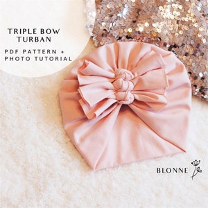 May include: A pale pink turban with a triple bow on top. The turban is made of a soft, stretchy fabric. The text "Triple Bow Turban" and "PDF Pattern + Photo Tutorial" is visible in the image.