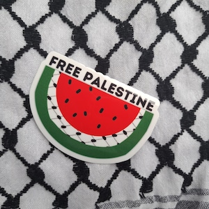 以下が含まれることがあります： 白と黒のパターンで覆われた背景に、スイカのデザインと「FREE PALESTINE」の文字が書かれたステッカーです。
