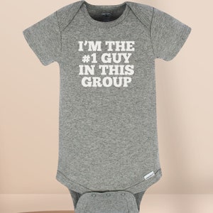 May include: A heather gray short-sleeved baby bodysuit featuring the white printed text I'M THE #1 GUY IN THIS GROUP centered on the chest. The garment has a crew neckline, short sleeves, and a bottom snap closure for easy access and dressing.