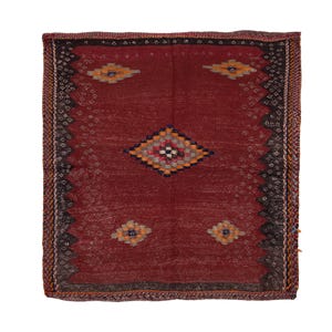 May include: A rectangular, hand-woven rug with a deep red field. The rug features geometric patterns in orange, yellow, blue, and black. The border is a darker shade with a repeating diamond pattern. The rug is approximately 36 inches by 48 inches.