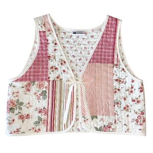 May include: A white quilted vest with a patchwork design featuring floral and plaid patterns in shades of pink and red. The vest has a tie closure and the label "WONDER & WONDER" is visible on the front.