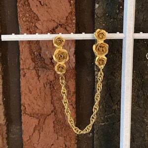 May include: A pair of gold-tone earrings with a chain connecting them. Each earring features three small rose-shaped charms.