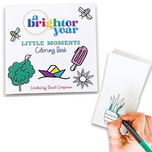 May include: A square coloring book titled A Brighter Year Little Moments with illustrations of bees, a tree, a paper boat, a popsicle, and a flower. A hand uses a green marker to color a potted plant illustration on an open page of the book.