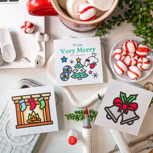 May include: Three square coloring cards featuring holiday illustrations. One card shows a fireplace with stockings, one shows two bells with a red bow, and the center card is titled Very Merry Mini Coloring Book with a tree, star, and mittens.