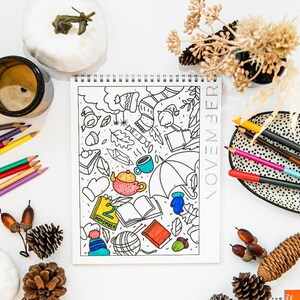 May include: A coloring book with a November theme featuring a variety of fall-themed illustrations, including leaves, acorns, a teapot, an umbrella, and a book. The book is open to a page with the date "2 November" written on it. The book is surrounded by colored pencils, pine cones, and other fall decorations.