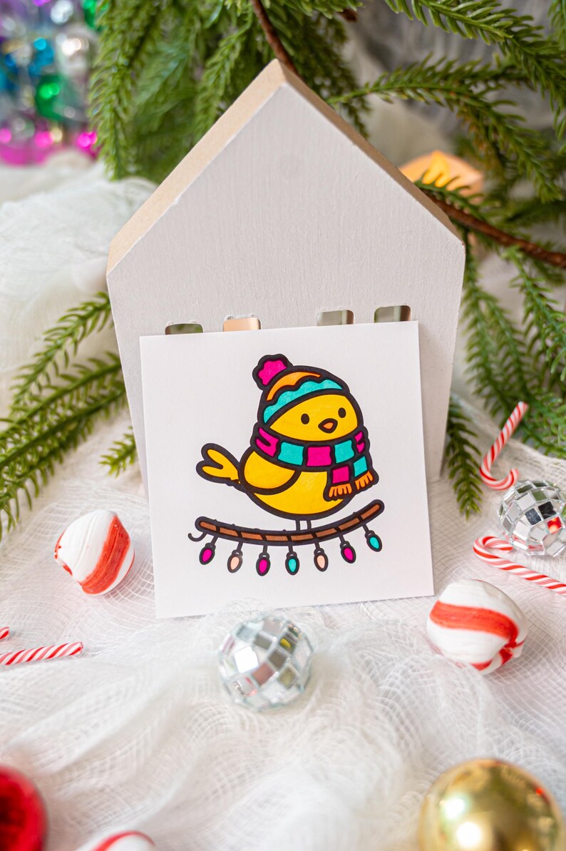 May include: A square white card featuring a cartoon illustration of a yellow bird wearing a teal and magenta striped winter hat and scarf. The bird is perched on a brown branch decorated with a string of small, colorful, glowing holiday lights.